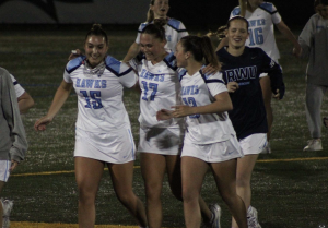 Three girls running, hugging each other, after a lacrosse game. 